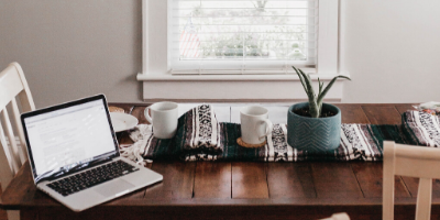 Laptop on kitchen table surrounded by mugs and plants